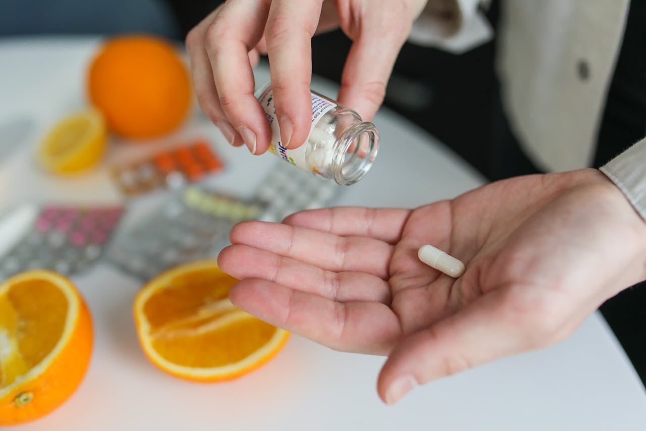 services-02 Close-up of a person taking a vitamin capsule with citrus fruit and medication on a table.