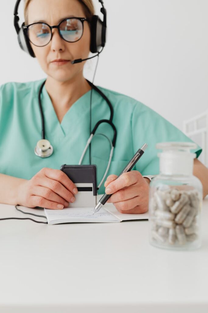pexels photo 7195111 Medical professional in green scrubs writes notes while on a call, with a focus jar of capsules.
