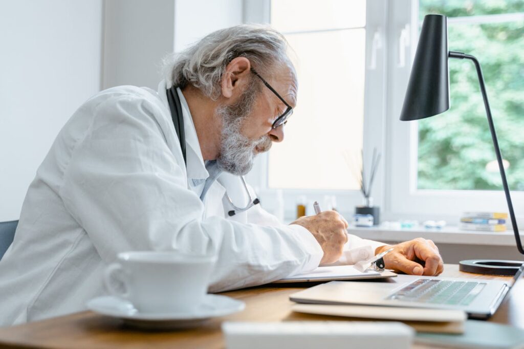 pexels photo 8376184 Elderly doctor writing notes at his desk with a focus on work in a well-lit office.